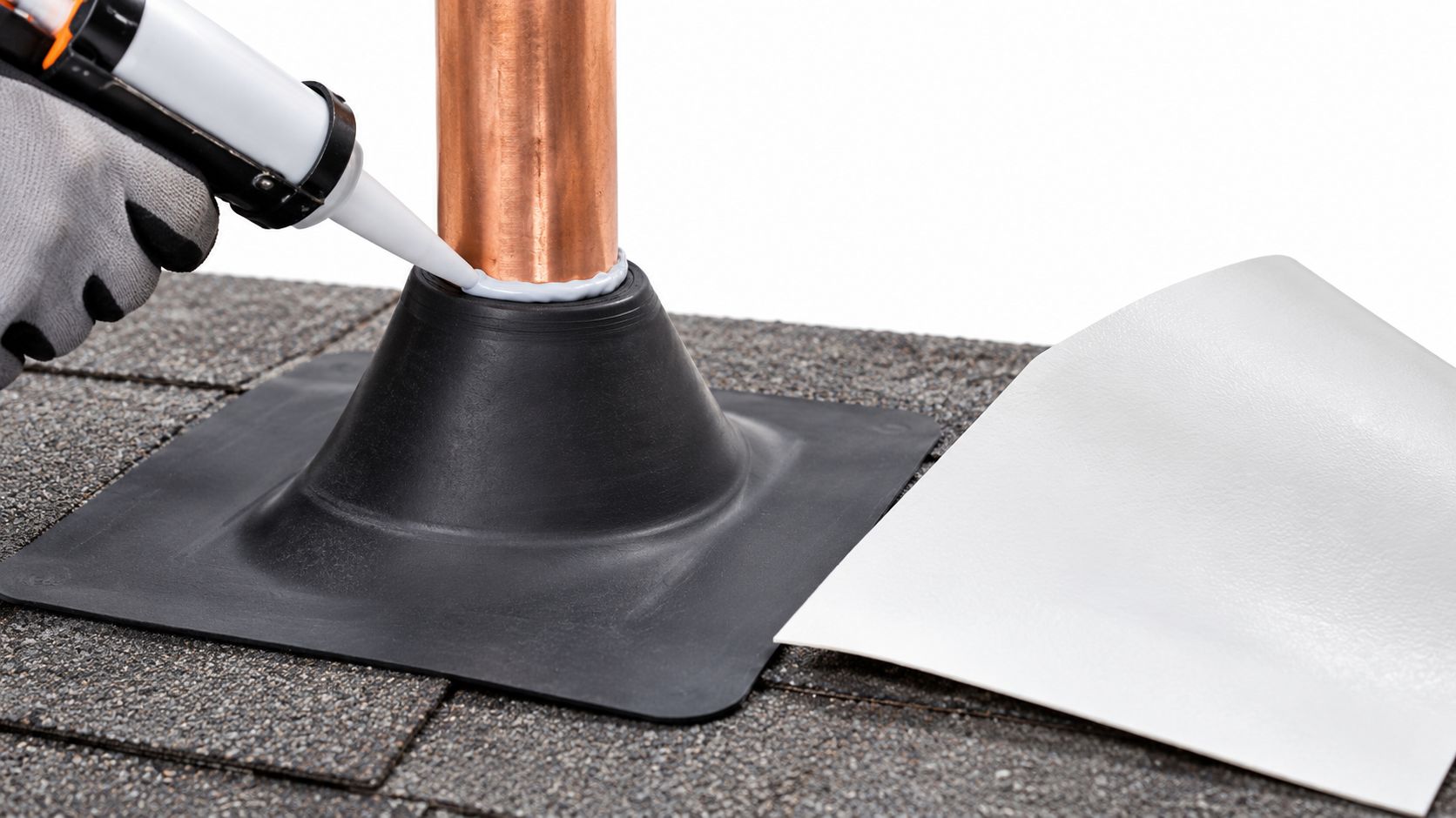 A gloved hand applies sealant to a roof pipe flashing boot on an asphalt shingled roof.